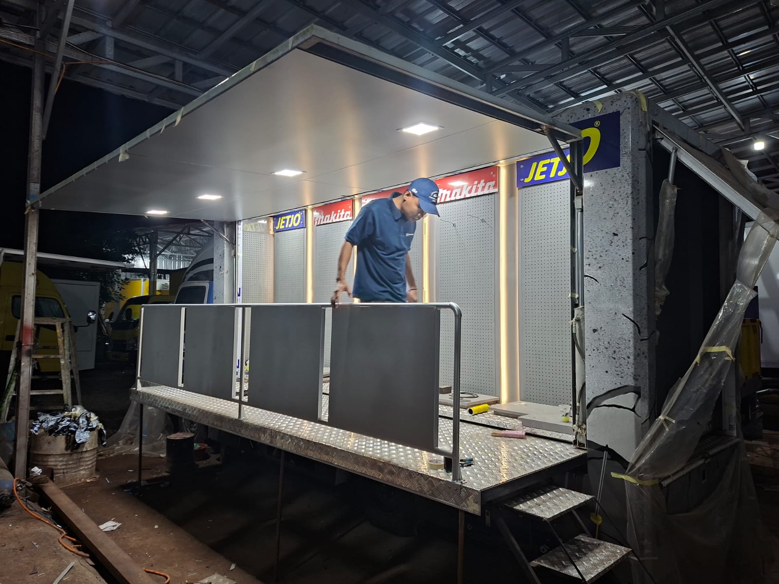 Mekanik sedang memeriksa pompa hidrolik pada rangka truk karoseri untuk memastikan tekanan stabil.